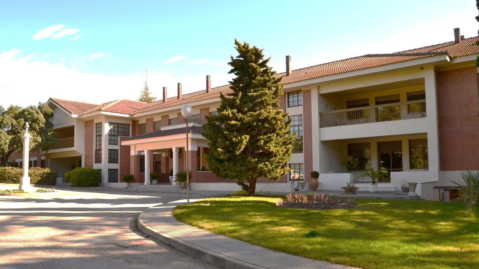 A red-brick school building with a lawn and trees on a sunny day
